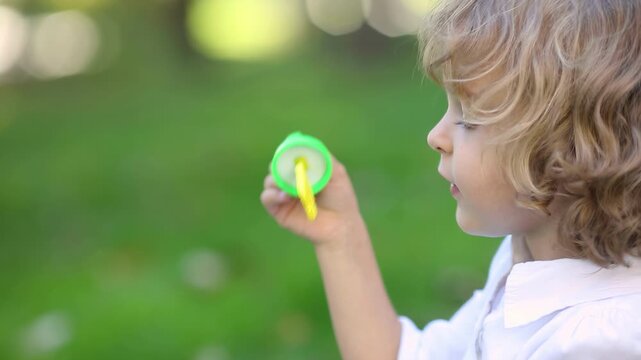 Happy child blows soap bubbles. Funny kid having fun outdoor. Little girl playing in the spring park. Slow motion