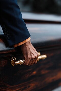 Pallbearer gripping ornate coffin handle during funeral service