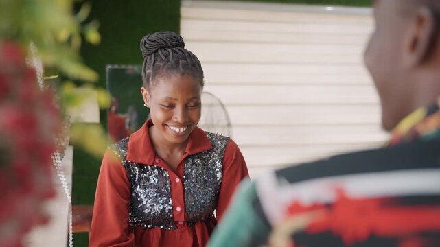 Black woman smiling at partner, creative designer woman responding with warm laughter, braided hairstyle and sequin vest, shy downward glance then bright smile, engaged listening and gentle nod,
