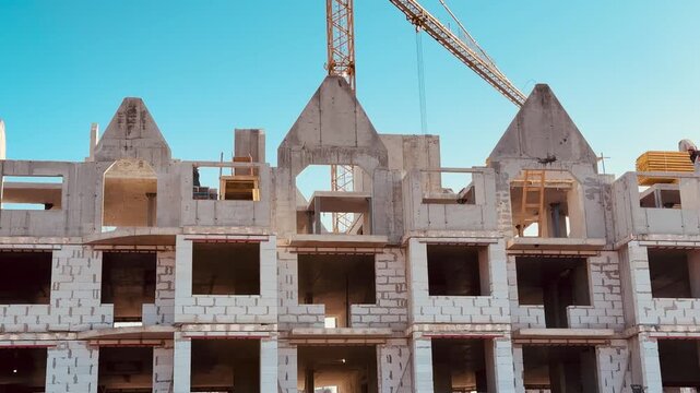 Aerated concrete apartment construction under blue sky, tower crane lifting blocks, exposed blockwork facade with triangular