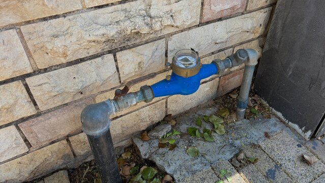 Blue water meter and pipes mounted on an outdoor brick wall, utility infrastructure concept for water consumption measurement
