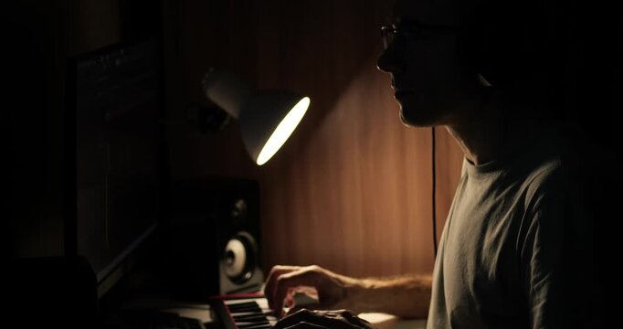 Music production in home studio. Musician creates beats using keyboard and software. Evening atmosphere enhances creativity and inspiration in workspace.