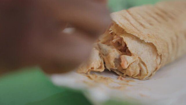 Closeup black mans hands holding shawarma on date night, fingers peeling flatbread, tender chicken chunks, tangy sauce, green tabletop, paper napkin, casual cafe vibe, warm city light, playful gesture