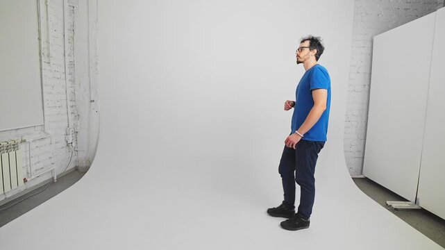 Bearded Caucasian guy is going with closed long umbrella waving it like a cane filmed in a studio. Confident young adult man is walking with device which can save him from the rain. Ready for overcast