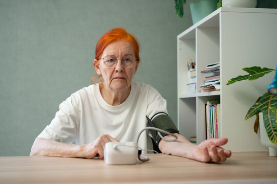 A senior woman seated at a table gives an interrogative, questioning glance towards the camera. curiosity or concern, a relatable moment in the context of health monitoring