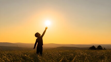 Fototapeta premium Young boy reaching towards sun in beautiful open grassy meadow