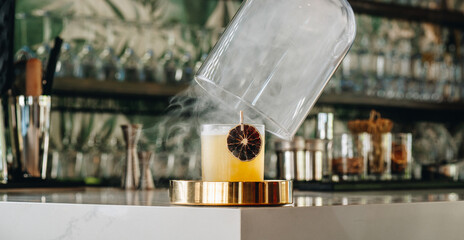Lifting glass cloche from smoking cocktail on bar. Action shot of a glass dome being lifted to reveal a smoking cocktail with dried citrus garnish. © Анна Терелюк