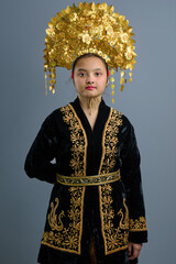 Naklejka premium Young Indonesian Asian Girl Portrait Wearing Ornate Gold Headdress and Embroidered Traditional Dress in Studio
