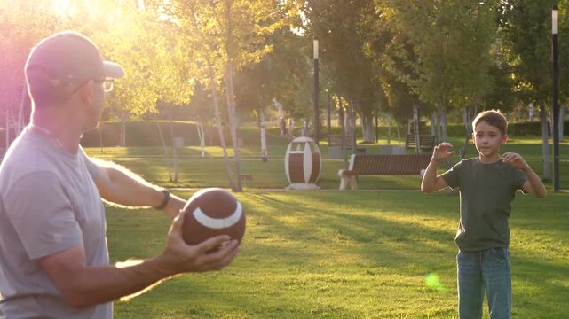 Father and son playing American football in park at sunset, passing ball and running on grass in warm golden light. Coaching, mentorship and active parenting. Healthy childhood and outdoor lifestyle.