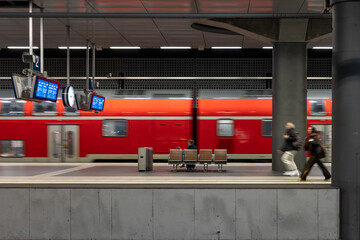 Red commuter train passing the platform. People waiting at modern station. © puhimec