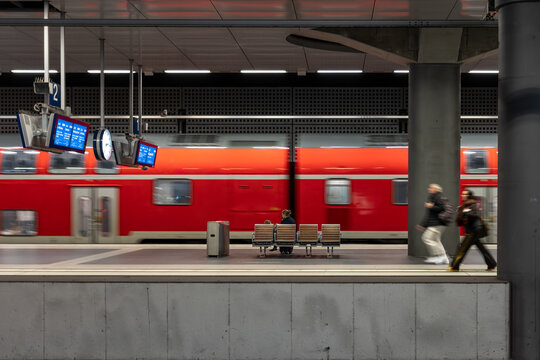 Red commuter train passing the platform. People waiting at modern station.