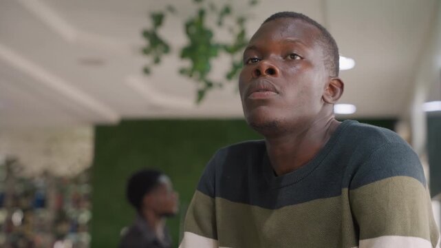 Black man in cafe waiting, striped sweater and greenery backdrop, contemplative expression, subtle nervousness and hopeful gaze, candid cinematic portrait capturing romantic anticipation and intimate