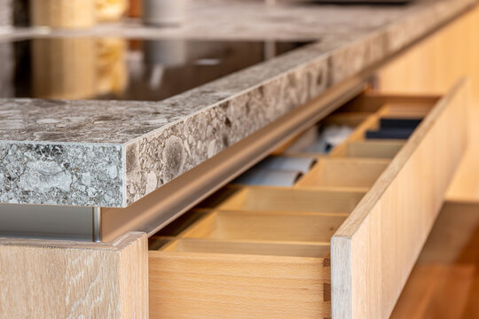 Organized kitchen island drawer made of wood. Detailed view of modern kitchen furniture.