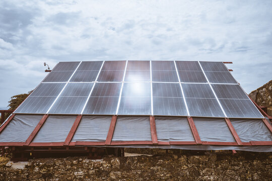 Large solar panel array mounted on rustic red wooden roof above old stone wall, blending renewable energy technology with rural architecture