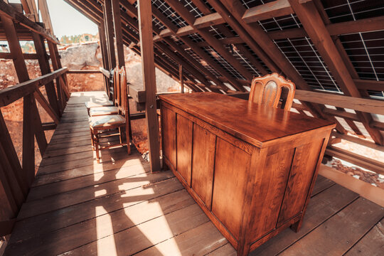 Attic walkway with vintage wooden desk and chairs under rustic roof structure, where dark solar panels are visible between warm wooden beams