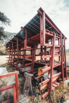 Red wooden lumber storage shed with stacked timber, solar panel roof and mounted speakers, blending rustic material storage with modern outdoor technology