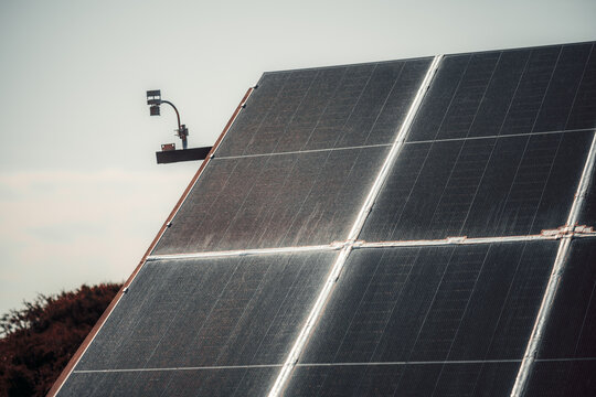 Telephoto close up of solar panels on a sloped roof with metal joints, soft sky background and industrial lamp, showing clean energy technology