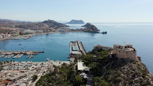 Aerial view of Aguilas city in Murcia, Spain, featuring Levante Bay and marina. Coastal urban landscape with calm Mediterranean waters, harbor structures and scenic shoreline.