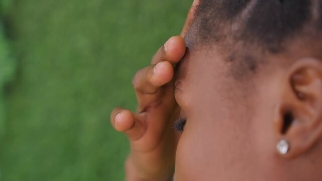 Side profile woman touching ear, braided hair and earring stud against green wall, intimate closeup showing poised nervousness, waiting glance with soft bokeh, natural light, delicate skin texture,