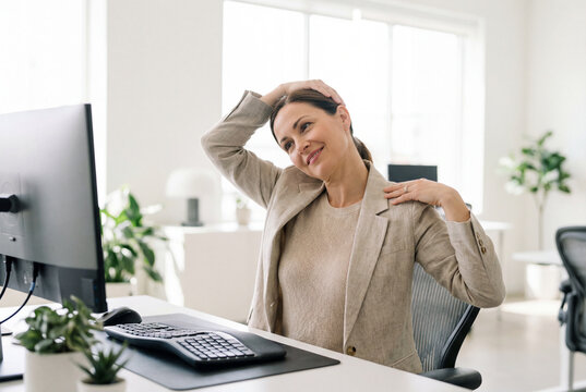 Woman doing a neck stretch exercise at her desk in a modern office workplace