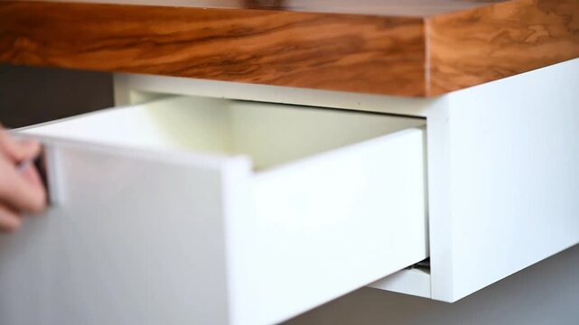 Woman's hand opening an empty white modern drawer with a wooden top in a close-up shot