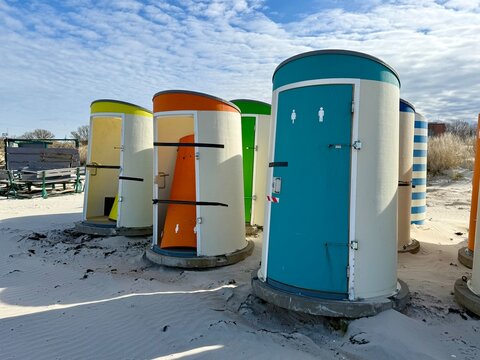 Colorful beach changing cabins on sandy shore under blue sky with textured clouds at seaside.