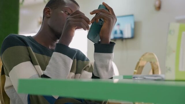 Young male notices upsetting text. Man in cafe discovers emotional message on device. Young individual sitting at cafe table reading distressing message with somber mood and subdued lighting