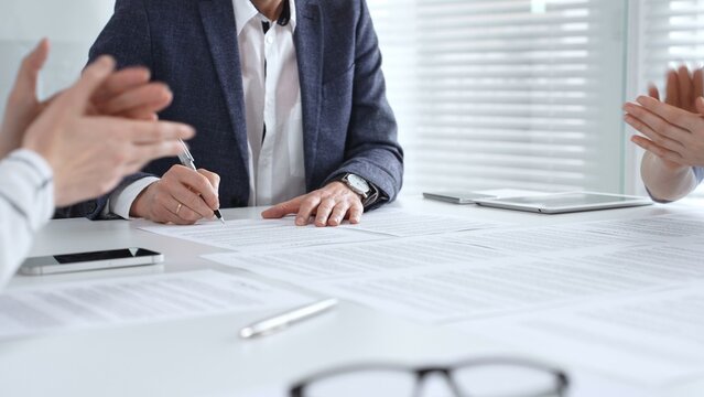 Business professional hand holding a pen, signing a document on a white desk during an important boardroom meeting, finalizing a partnership or legal agreement