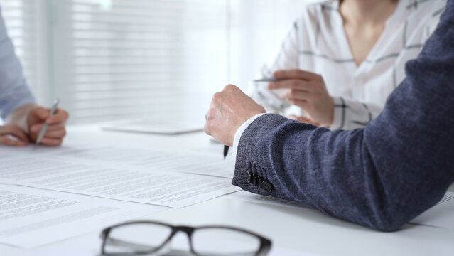 Business professionals reviewing contract documents and discussing terms during a corporate meeting, focusing on agreement details and signature importance for legal finalization