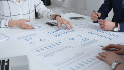 Business team in a conference room reviewing financial reports, charts and graphs across the table, collaborating on strategy, investment planning and growth initiatives © volha_r