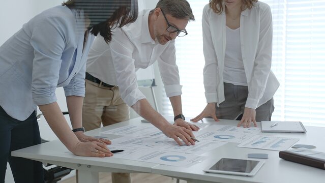 Business professionals collaborating around a modern office table, reviewing charts and reports, brainstorming strategy and data driven decisions to drive growth and team performance