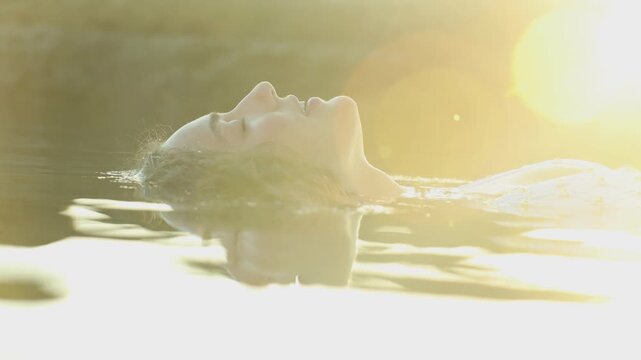 Closeup of a serene woman floating in water at sunset in slow motion. Woman in a relaxed flow state of mind.