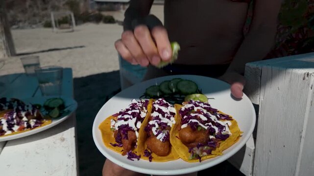 Mature woman squeezes lime on a delicious shrimp tacos at a beach side taco stand in Baja California Mexico.