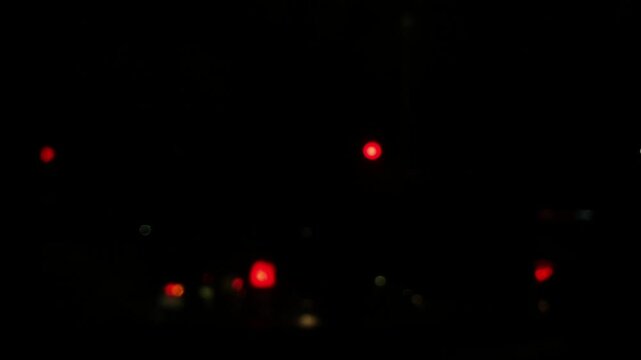 Blurry red and white city traffic lights float in the dark night. Forward camera movement captures abstract bokeh circles glowing and shifting on an urban road.