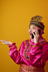 Naklejka premium Indonesian Asian Woman in Pink Traditional Costume and Hijab Talking on Phone With Surprised Expression