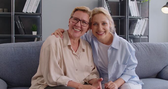 Senior mother and daughter hug and smile on sofa. At home, they sit close in a modern living room, sharing trust and comfort. Family unity, loce, care, relationship and warmth concept.