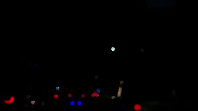 Defocused colorful traffic lights scatter across the dark night landscape. Forward movement brings bright glowing bokeh circles closer to the camera in a moody urban setting.