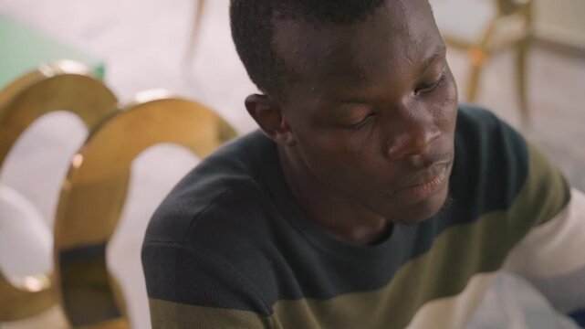 Black man pensive after quiet date, young black writer reviewing notes on chair, staring at empty cup, subtle head tilt, pen resting, memory replay, soft amber light, film texture, introspective