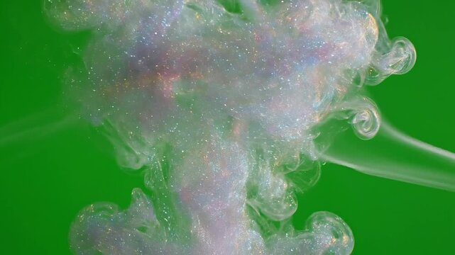 Iridescent glitter and paint swirls in water creating a mesmerizing abstract cloud against a vibrant green background.