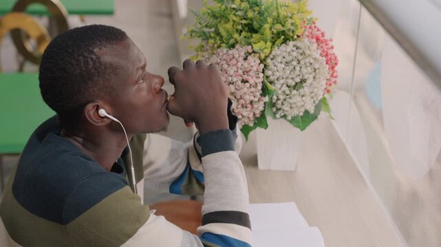 Cafe patron lost in thoughts. Man sitting with headphones at cafe. Thoughtful man enjoying moment with flowers nearby. Cinematic scene of man lost in imagination with hydrangeas close