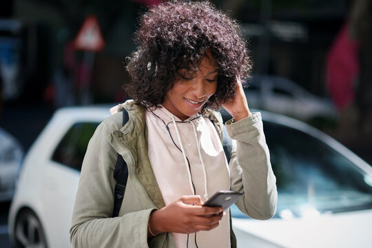 Streaming, headphones or black woman in city with phone, song connection or listening to music playlist. Smile, digital or female person with tech, online track or radio subscription on audio app.