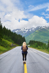 Obraz premium Back, woman and hiking on road with mountains, sightseeing trip and travel exploration for vacation. Person, backpack and adventure outdoor with scenery for winter holiday, peace or tourist trekking.