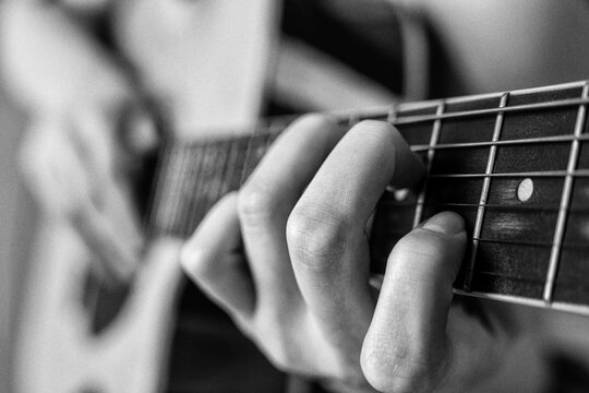 Woman playing acoustic guitar. Closeup of hand on fretboard. Monochrome musical instrument performance. Retro style vintage photography with grain and soft focus, depth of field