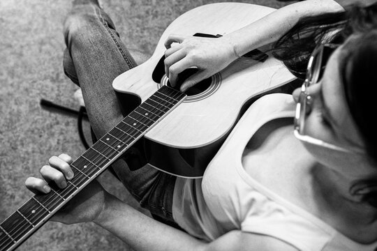 Woman playing classic guitar. Young lady practicing music at home. Musician enjoying hobby. Black and white vintage photography with film grain, soft blur. Artistic lifestyle concept. High angle view
