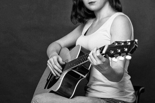Young woman playing Spanish six string acoustic guitar in retro style. Monochrome photography with film grain and selective focus. Hobby, creativity and music education concept