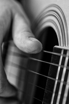 Musician hand playing acoustic guitar string. Extreme closeup shot of thumb finger touching instrument cord. Monochrome photo with retro style, noise and analog film grain effect
