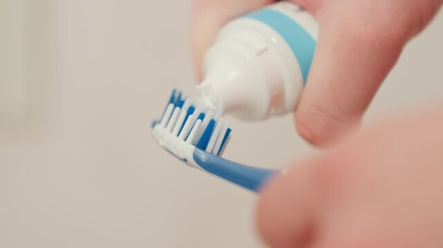 Brushing preparation in bathroom. Hand applies mint paste to toothbrush bristles. Individual carefully applies mint flavored toothpaste from tube onto toothbrush for morning dental hygiene