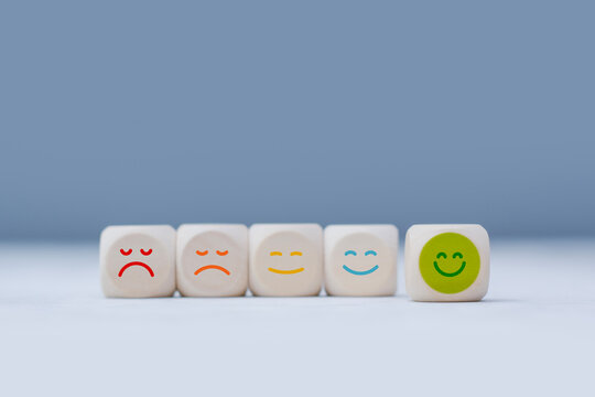 Minimal customer satisfaction concept showing wooden cubes with sad, neutral and happy emoji faces arranged from low to high rating. Concept feedback surveys, service quality and customer experience.