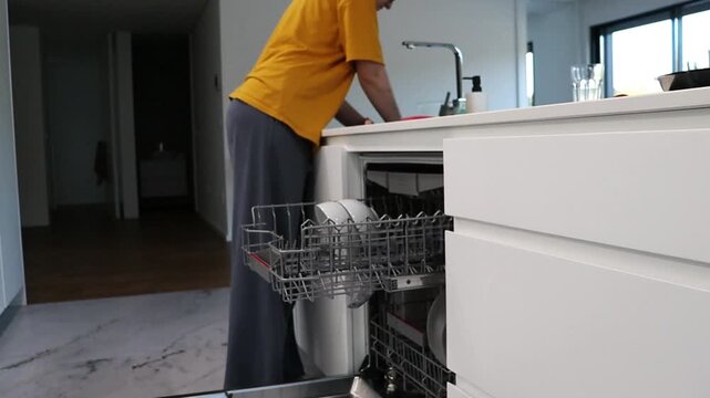 Woman loading dishes into dishwasher rack in modern kitchen. Household cleaning routine for appliance use, organizing tableware, dish washing process and home care