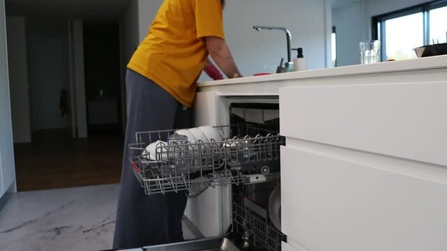 Woman loading dishes into dishwasher rack in modern kitchen. Household cleaning routine for appliance use, organizing tableware, dish washing process and home care concept.